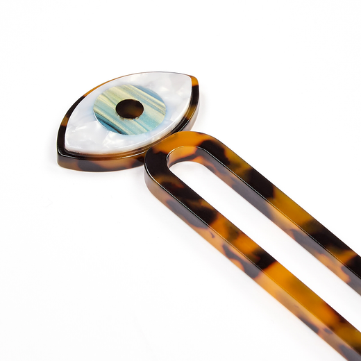 Detail of a chignon pin topped with an eye shaped decorative detail.